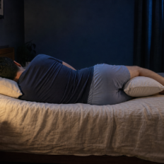 An adult testing a side-sleeping setup with natural pillow compression and a pillow between the knees.